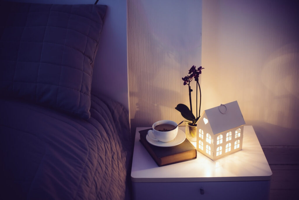 clutter free nightstand with a book, a cup of tea, night light and a flower