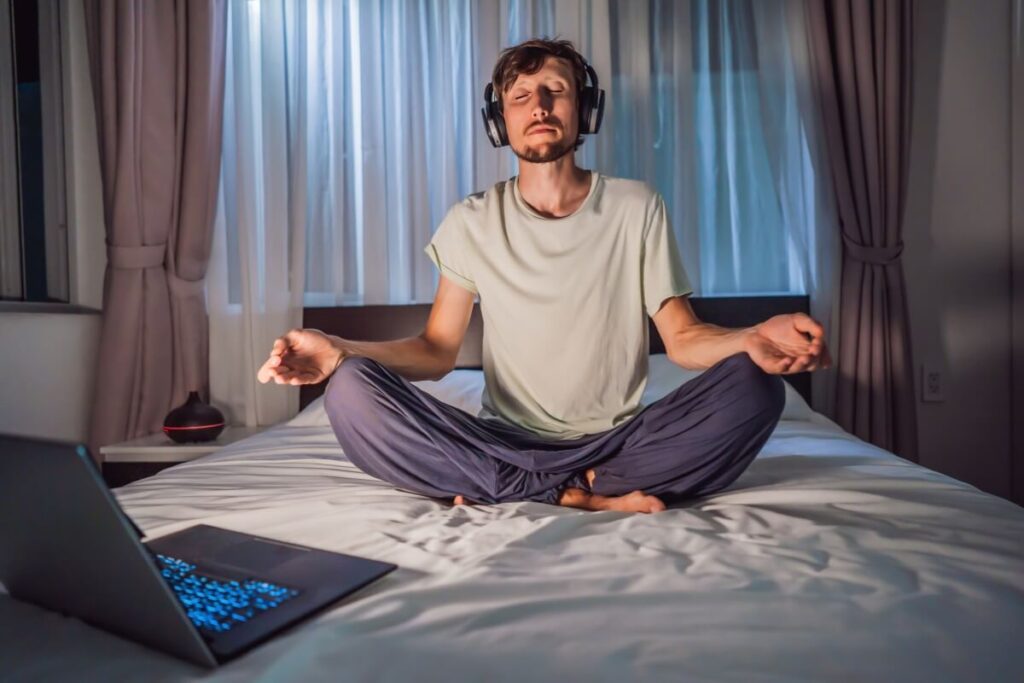 a man meditating on a bed using a meditation app on a lap top 