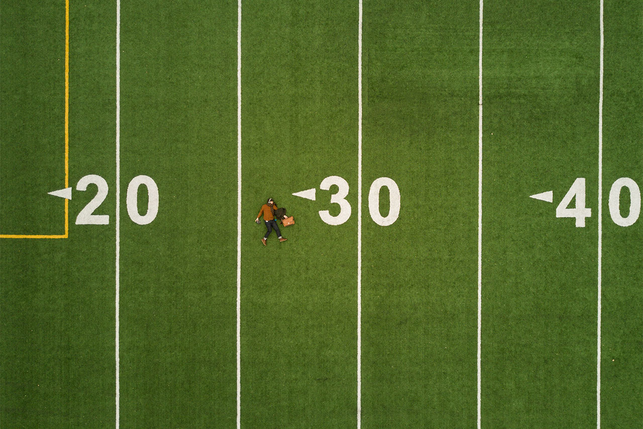 Aerial view of a lone figure on a football field representing midlife personal philosophy and transition