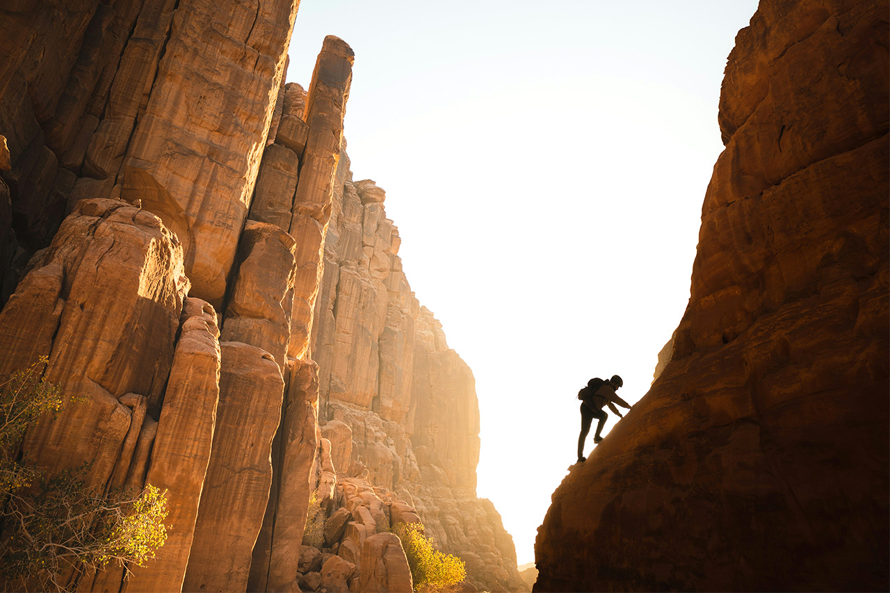 Silhouette of a climber scaling a rock face in a desert canyon at sunset